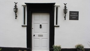 Une porte blanche avec des moulures noires, une enseigne noire indiquant « CHURCH FARMHOUSE B&B », et deux lanternes fixées au mur.