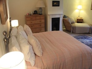 Ein Schlafzimmer mit einem Bett, Nachttischlampen, einem Schminktisch, einem Kamin und einem Sessel.