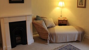Une chambre confortable avec une cheminée, un lit recouvert d’un plaid, une table de chevet avec une lampe et un tableau encadré au mur.