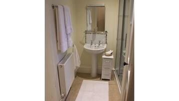 A small bathroom with a white sink, a mirror, a towel rack, a small drawer unit, and a glass shower enclosure.