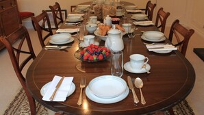 Une table à manger dressée pour un repas, avec des assiettes, des couverts et un saladier de fruits.