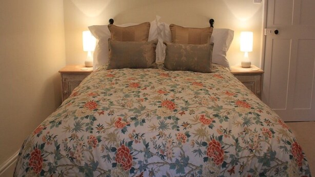 Une chambre à coucher avec une couvre-lit à motifs floraux, deux lampes de chevet et trois tableaux encadrés accrochés au mur.