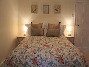 A bedroom with a floral bedspread, two bedside lamps, and three framed pictures on the wall.