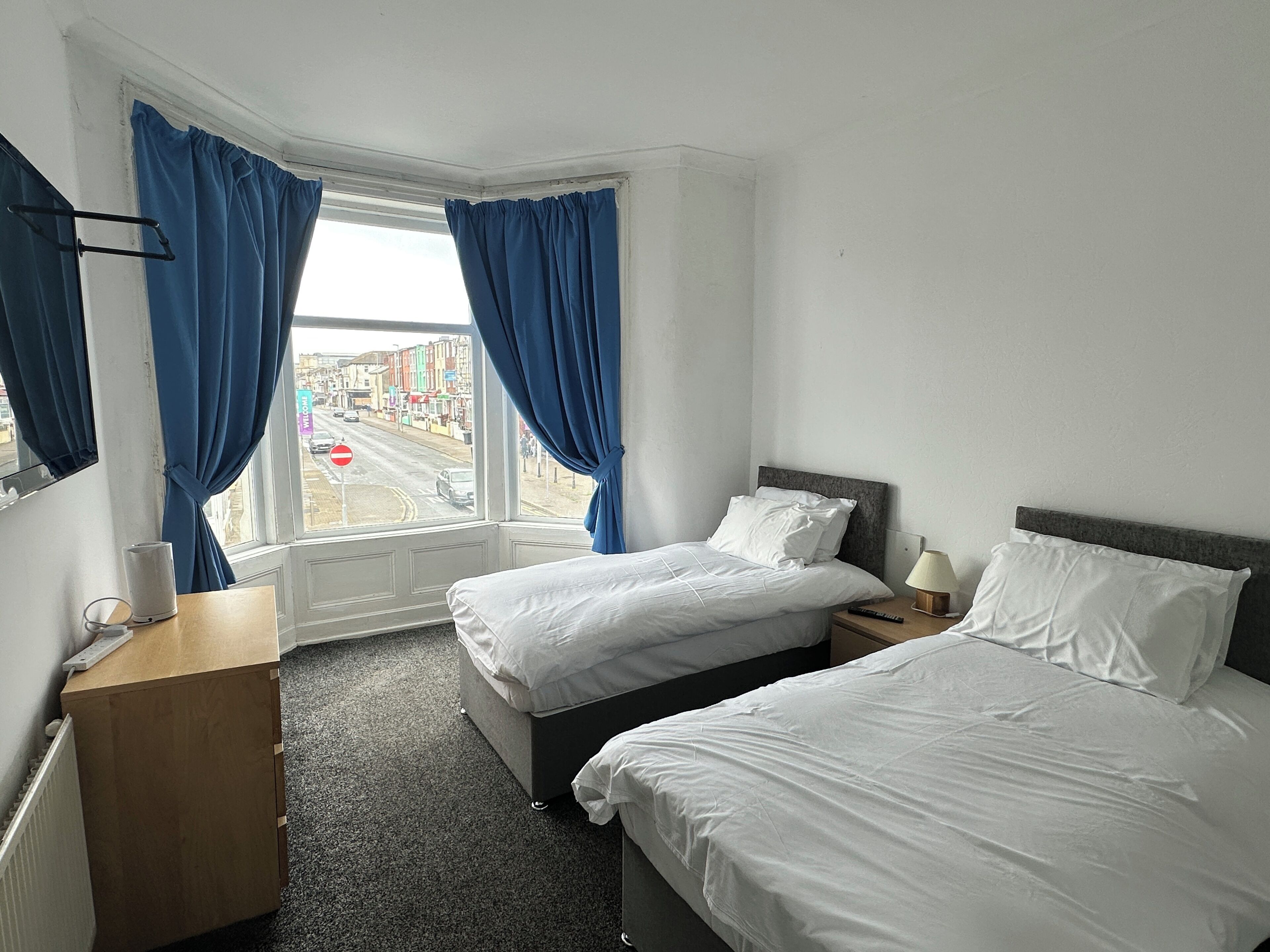 Une chambre d’hôtel avec deux lits, un bureau, une chaise, une fenêtre avec des rideaux et une vue sur la rue.