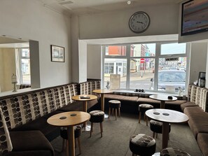 Um café com relógio, mesas e vista para a rua.