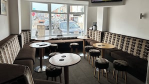 A cafe with a large window, seating area, and a wall-mounted TV. - Avari Beach Hotel (Blackpool)