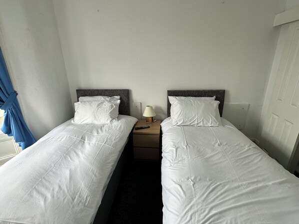 A room with two single beds, a bedside table with a lamp, and a blue curtain.