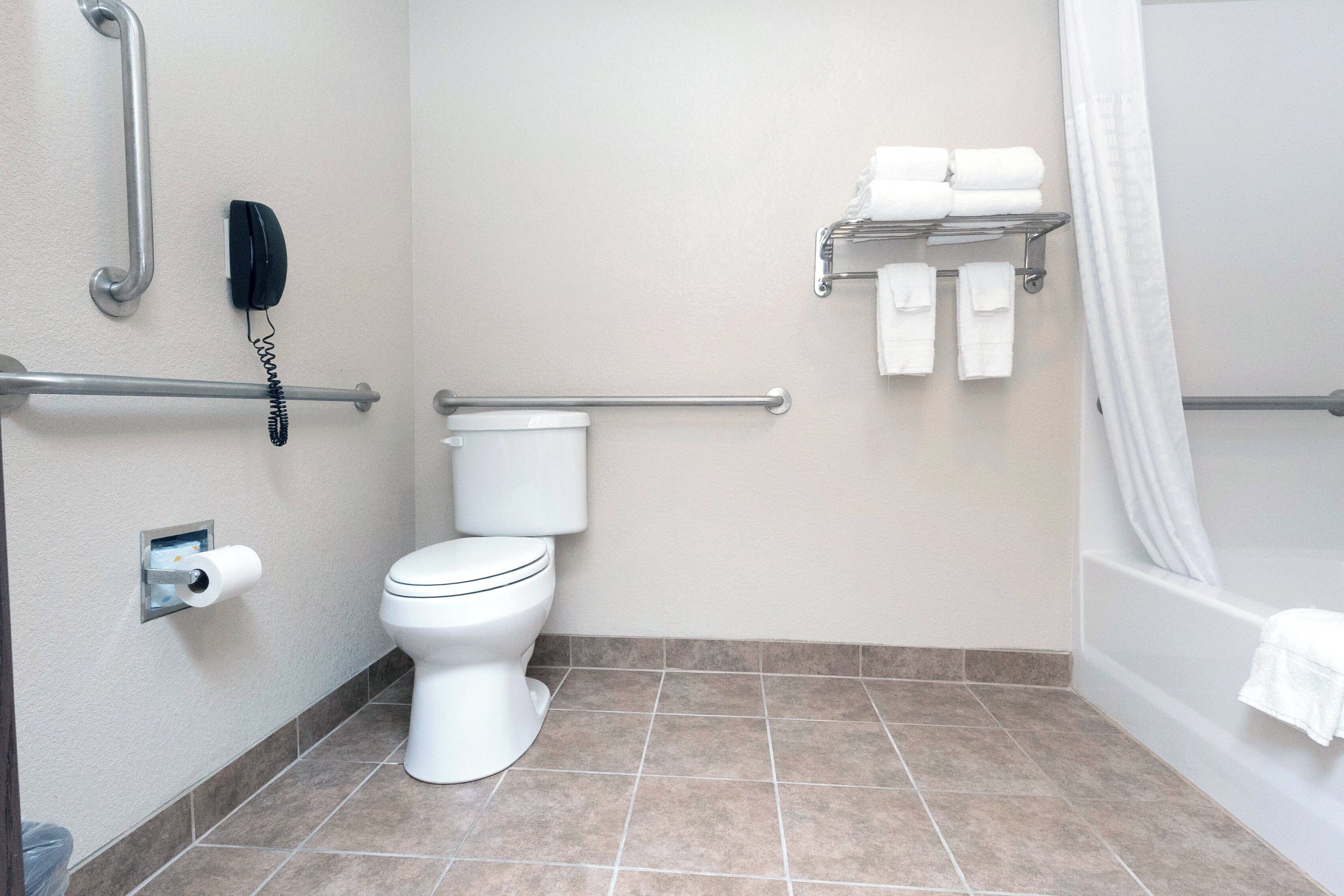 A bathroom with a toilet, a handrail, a telephone, and a towel rack.