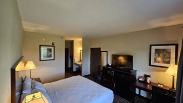 Habitación de hotel con una cama grande, un escritorio con televisor, un aparador y un baño a la vista al fondo.