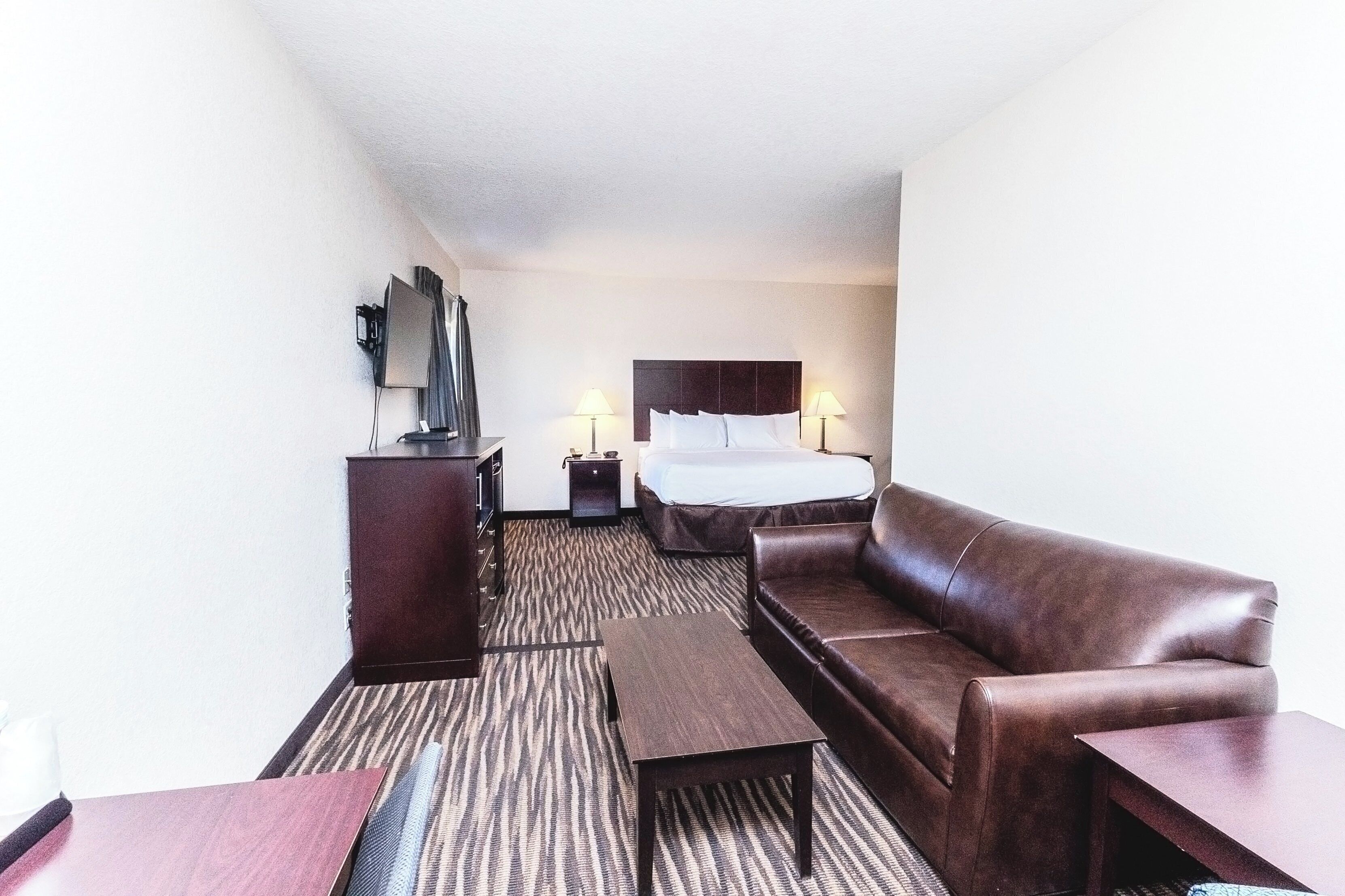 A hotel room with a bed, a leather sofa, a small table, a nightstand, and a TV.