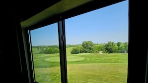 Une vue à travers une fenêtre donnant sur un terrain de golf, avec un ciel dégagé.