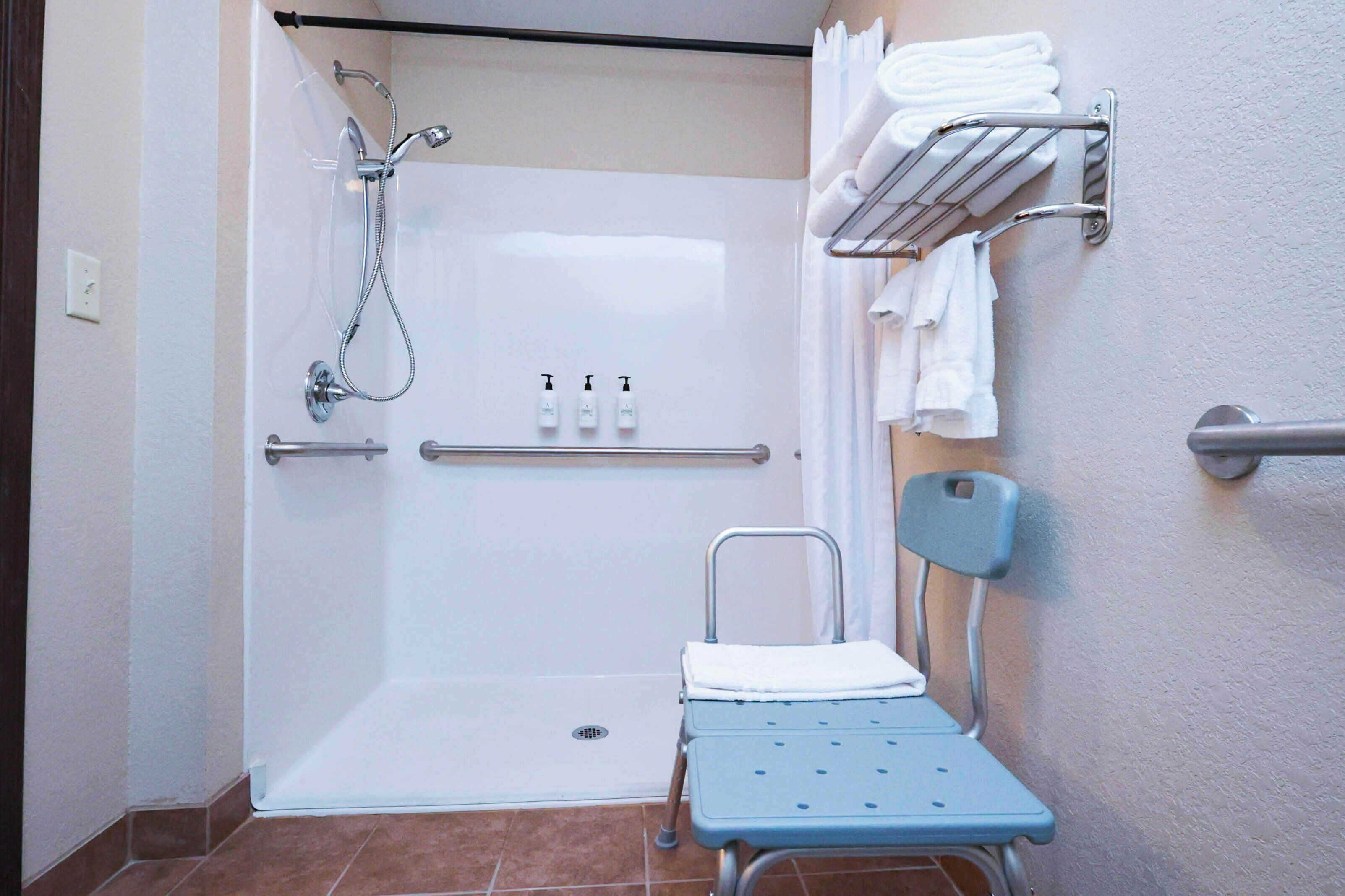 A shower area with a grab bar, a bench, and a towel rack with towels.