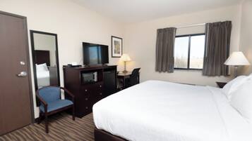Habitación de hotel con cama, escritorio, silla, televisión y ventana con cortinas.
