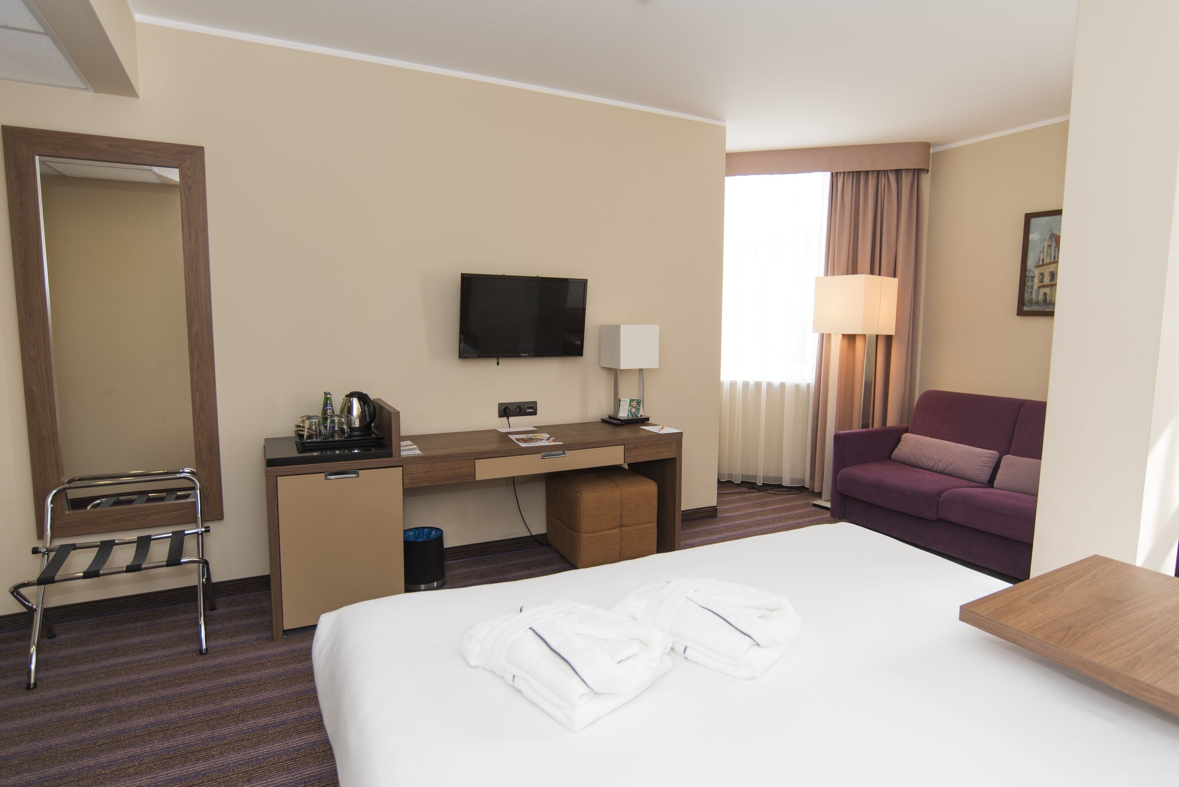 A hotel room with a bed, a desk, a television, a sofa, and a window with curtains.