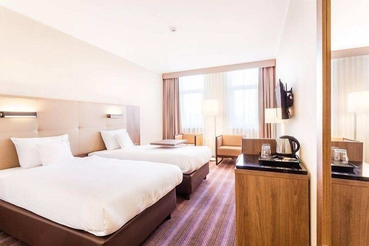 A hotel room with two beds, a desk with a coffee maker, a chair, and a TV on the wall.