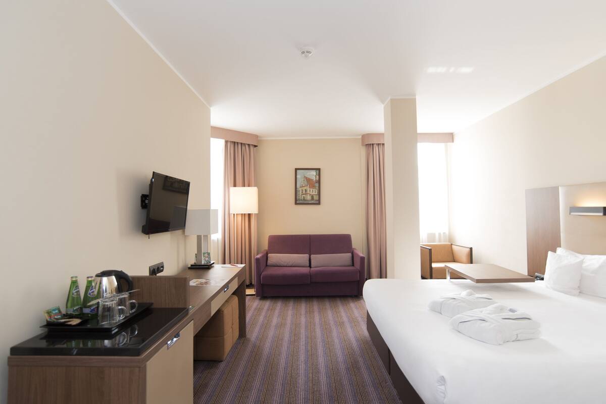 A hotel room with a bed, a sofa, a desk with a flat-screen TV, and a coffee station.