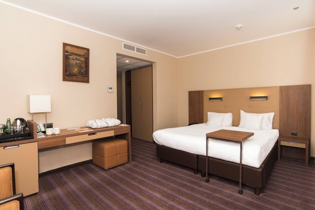 A hotel room with a bed, bedside table, desk, and a small seating area.