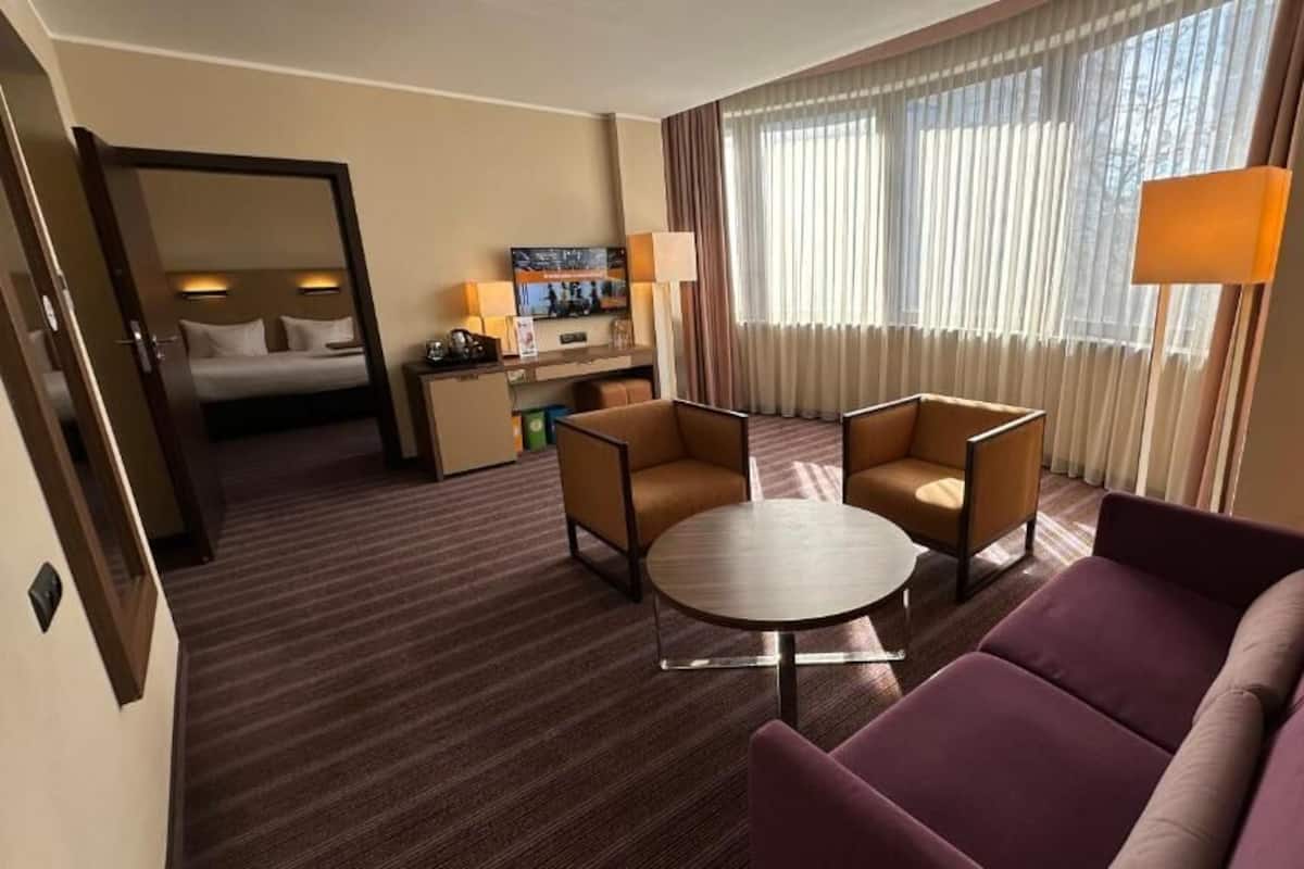 A hotel room with a bed, a desk with a computer, two armchairs, a round table, and a sofa.