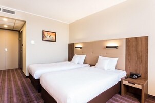Habitación de hotel con dos camas, cabecero de madera, mesita de noche con teléfono y un cuadro en la pared.
