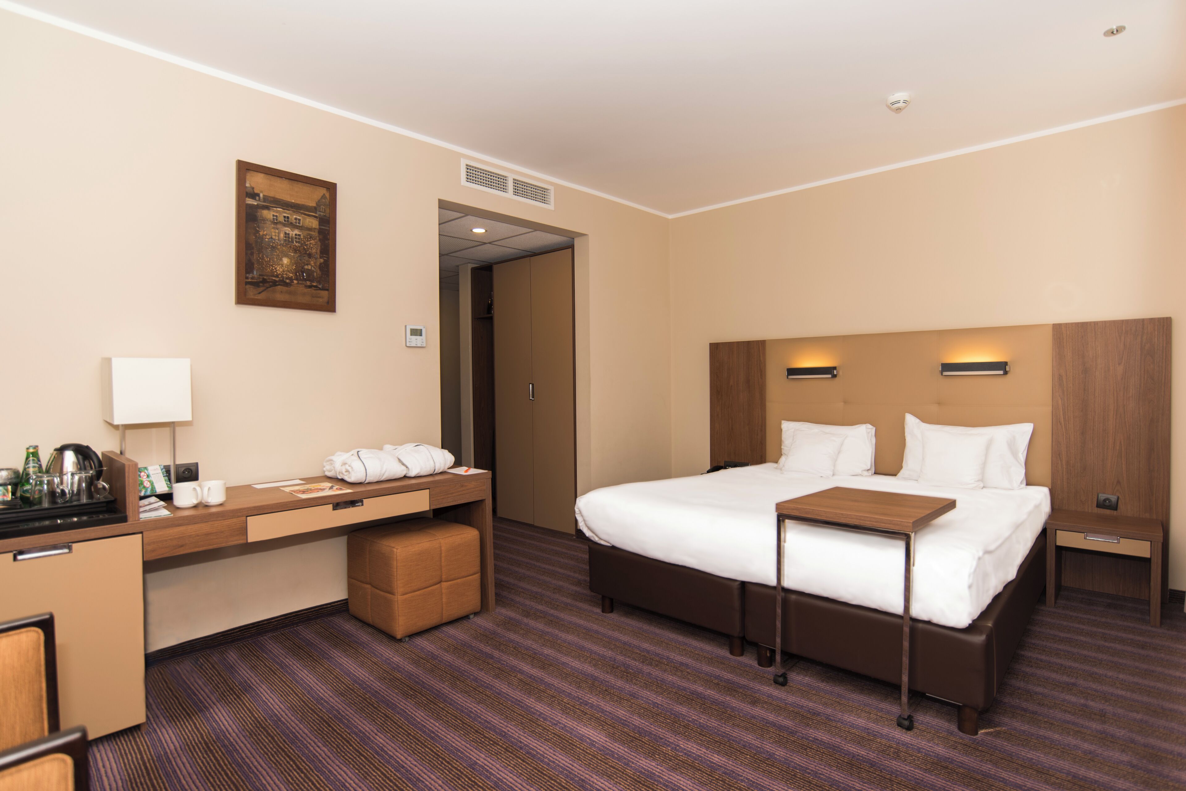 A hotel room with a bed, bedside table, desk with a lamp, and a small seating area.