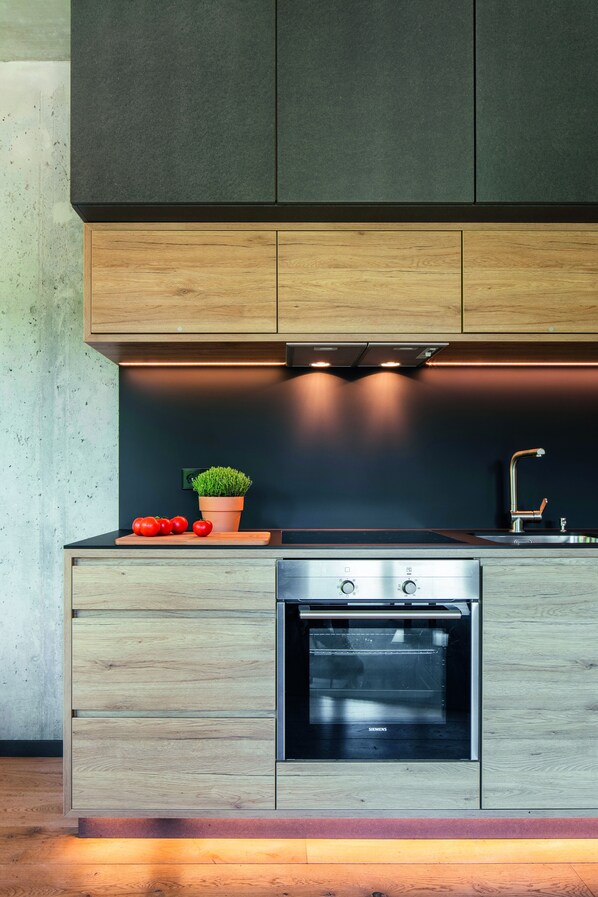A modern kitchen with wooden cabinets, a built-in oven, and a countertop with a potted plant and tomatoes.