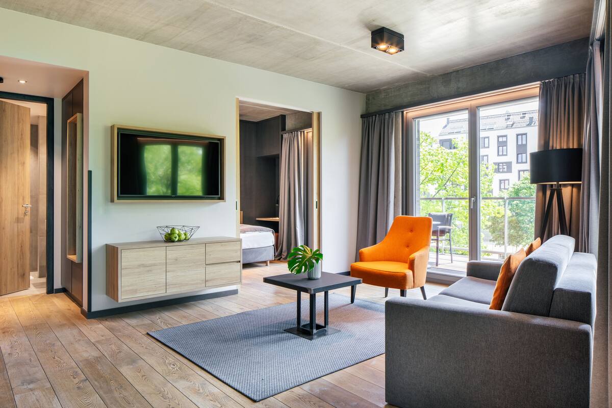 A modern living room with a sofa, armchair, TV, and a small table with a plant.