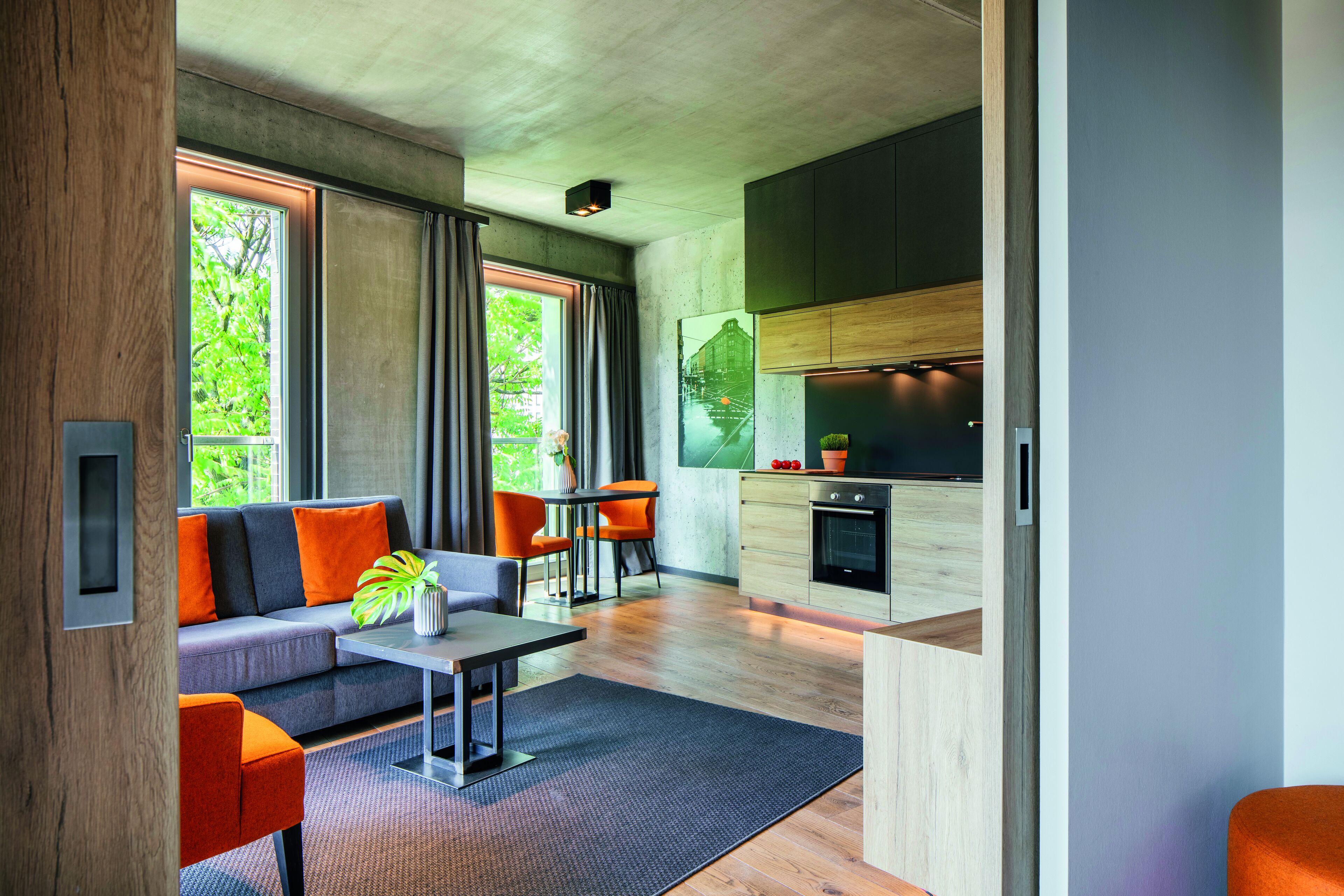 A modern living room with a sofa, coffee table, and chairs, a dining area with a table and chairs, and a kitchen with wooden cabinets and appliances.