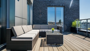 Una terraza en la azotea con un área de estar moderna al aire libre, que incluye un sofá y una mesa de centro, y un ventanal con vistas a la ciudad.