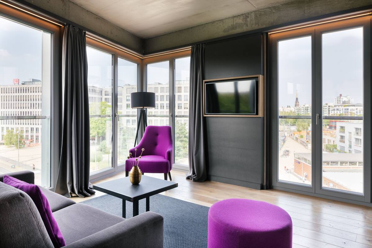 A modern living room with a sofa, armchair, and ottoman, a coffee table, and a TV mounted on the wall.