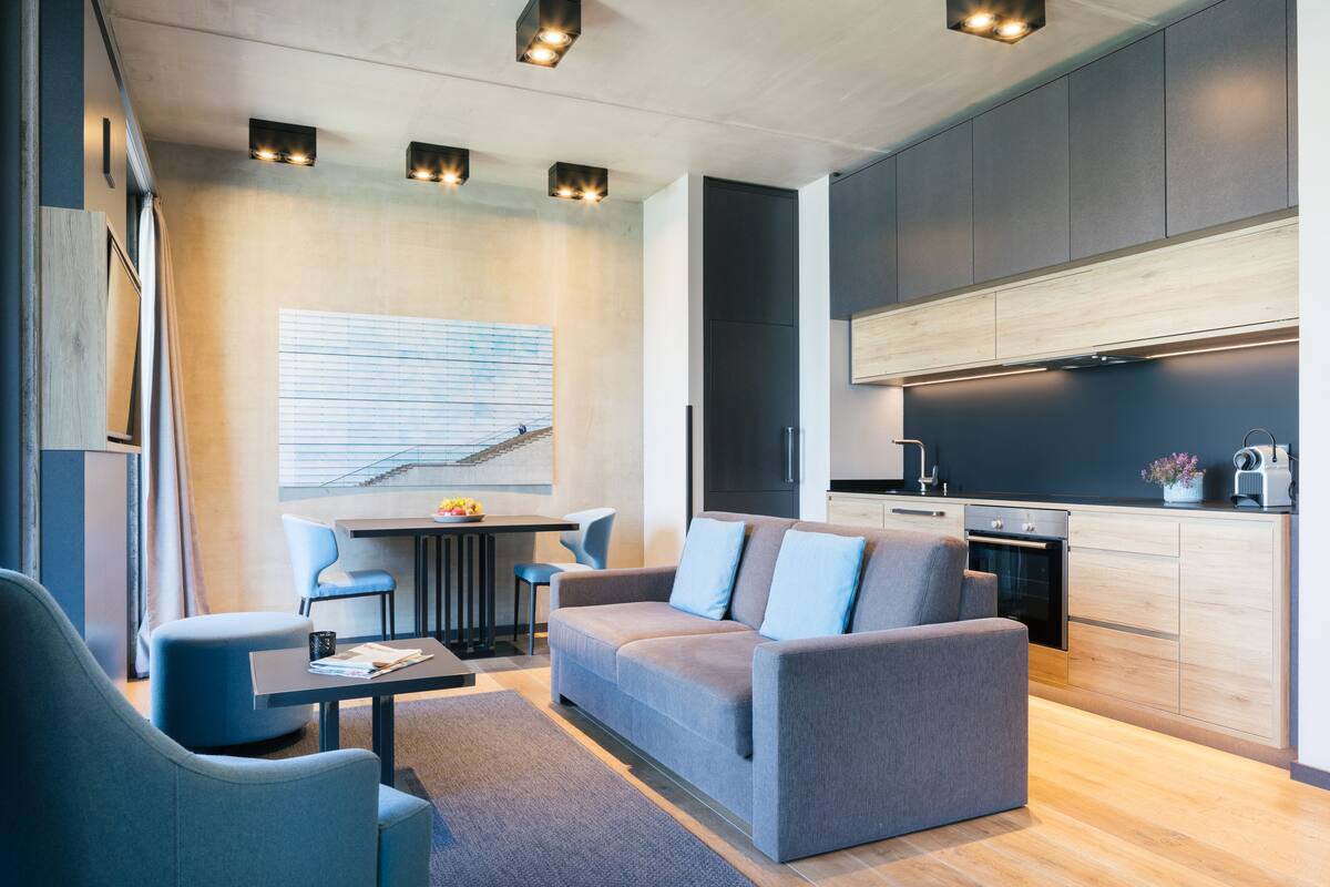 A modern living room with a sofa, chairs, a dining table, and a kitchen area with cabinets and appliances.