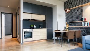 Una cocina moderna con armarios oscuros, encimera de madera y horno integrado. Hay una zona de comedor con una mesa y sillas, además de una estantería llena de libros.