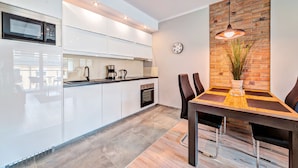 A modern kitchen with white cabinets, a built-in microwave, and a dining area with a wooden table and chairs. - Apartamenty Homely Place City (Poznan)