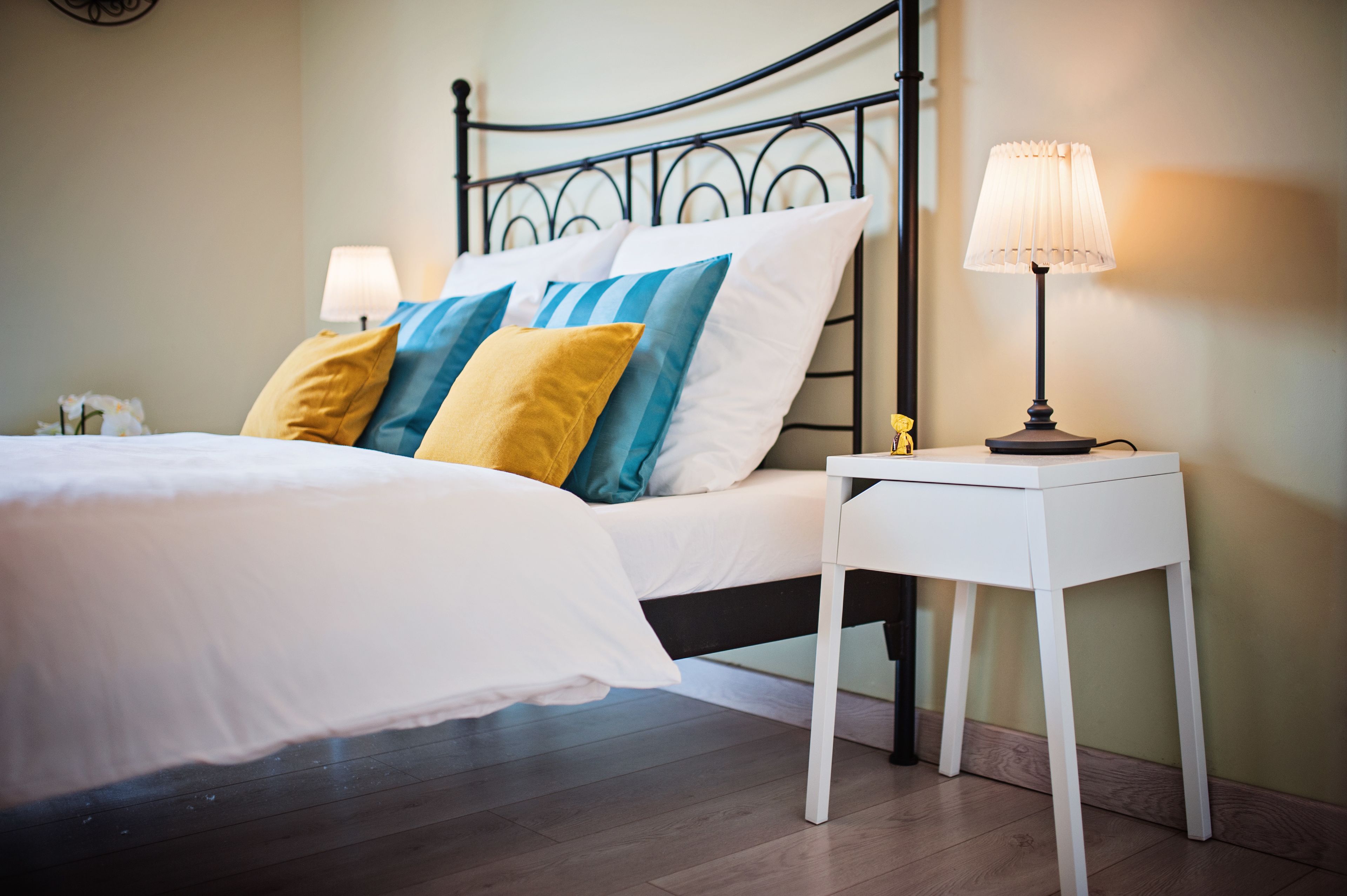 Un lit bien fait, avec une literie blanche et des coussins colorés, une table de chevet avec une lampe et une tête de lit moderne en métal.
