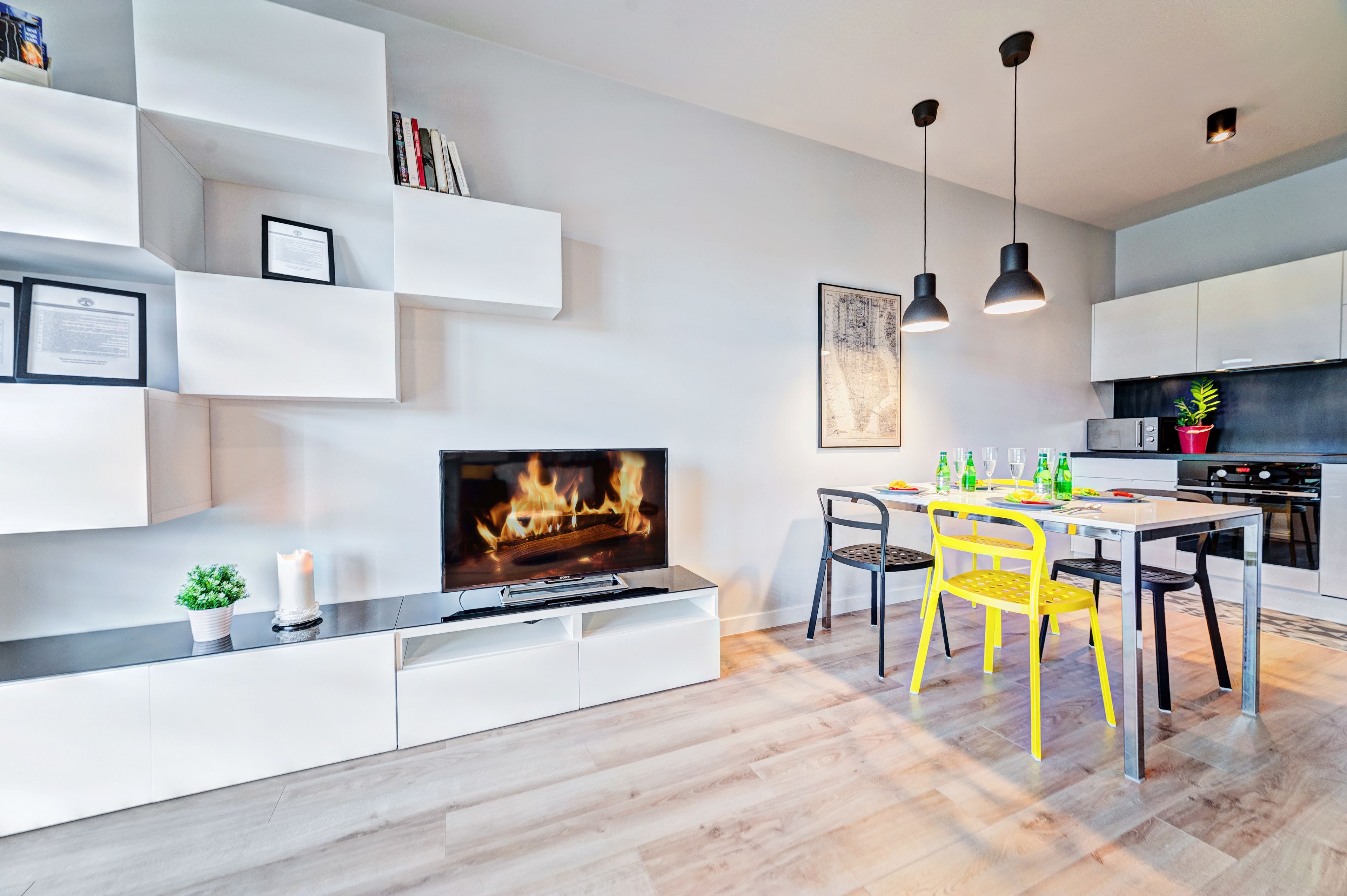 Una cocina moderna con comedor, muebles blancos y un televisor de pantalla plana mostrando una chimenea.