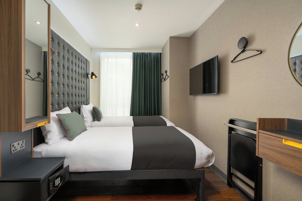 Ein modernes Hotelzimmer mit einem großen Bett, einem Fernseher, einem Spiegel und einem Nachttisch.