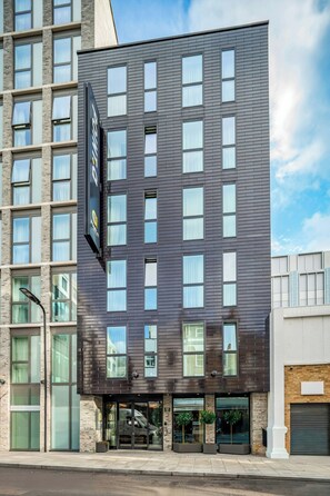 Ett modernt hotell med en mörk fasad, stora fönster och en väl synlig skylt.