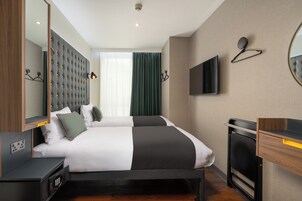 Ein Hotelzimmer mit einem großen Bett, einem an der Wand befestigten Fernseher, einem Spiegel und einem Nachttisch aus Holz.