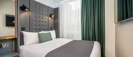 A modern hotel room with a large bed, a headboard with lights, a bedside table with a phone, and a large window with curtains.