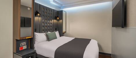 Une chambre d’hôtel moderne avec un grand lit, une table de chevet avec une lampe, un téléviseur à écran plat fixé au mur et une prise électrique sur le mur.