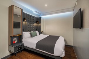 Ein modernes Hotelzimmer mit einem großen Bett, einem Nachttisch mit Lampe, einem flachbildfernseher an der Wand und einer Steckdose.