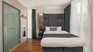 A modern hotel room with a large bed, a glass shower enclosure, a vanity with a mirror, and a nightstand. - Point A London Shoreditch (London)