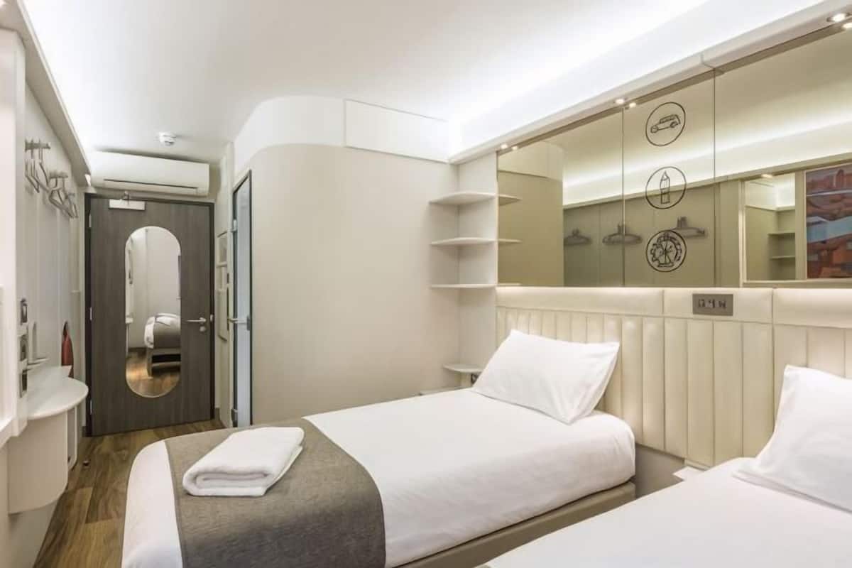 Ein Hotelzimmer mit zwei Betten, einem Spiegel, einem Heizkörper und einem Ablagefach mit Toilettenartikeln.