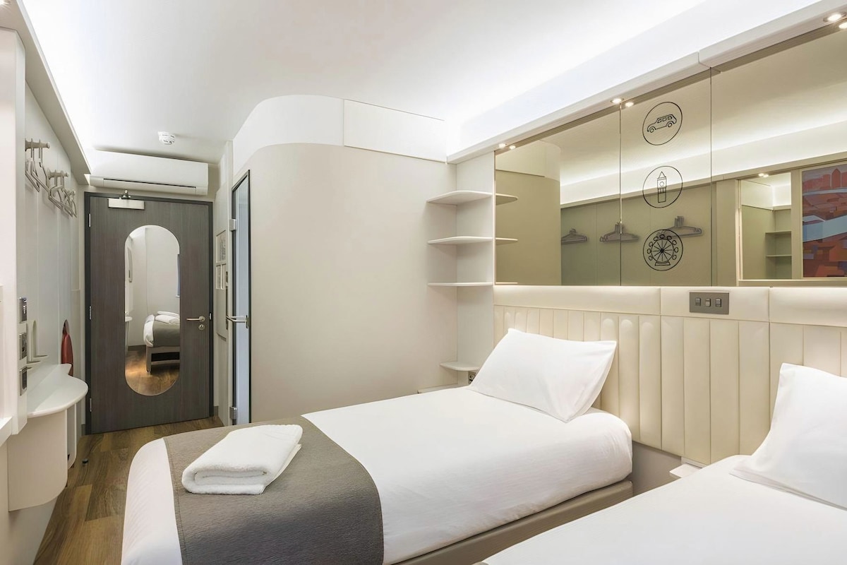 Une chambre d’hôtel moderne équipée d’un lit, d’un miroir, d’une armoire et d’une salle de bain.
