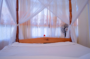 A bed with a wooden headboard, white bedding, and sheer curtains. - Stardom Hotel (Nairobi)