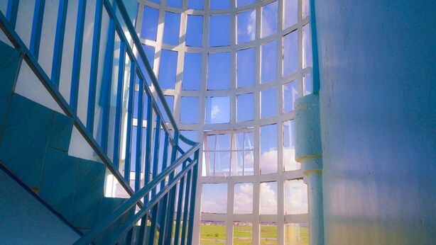 A staircase with blue railings leading to a large window with a view of a green landscape. - Stardom Hotel (Nairobi)