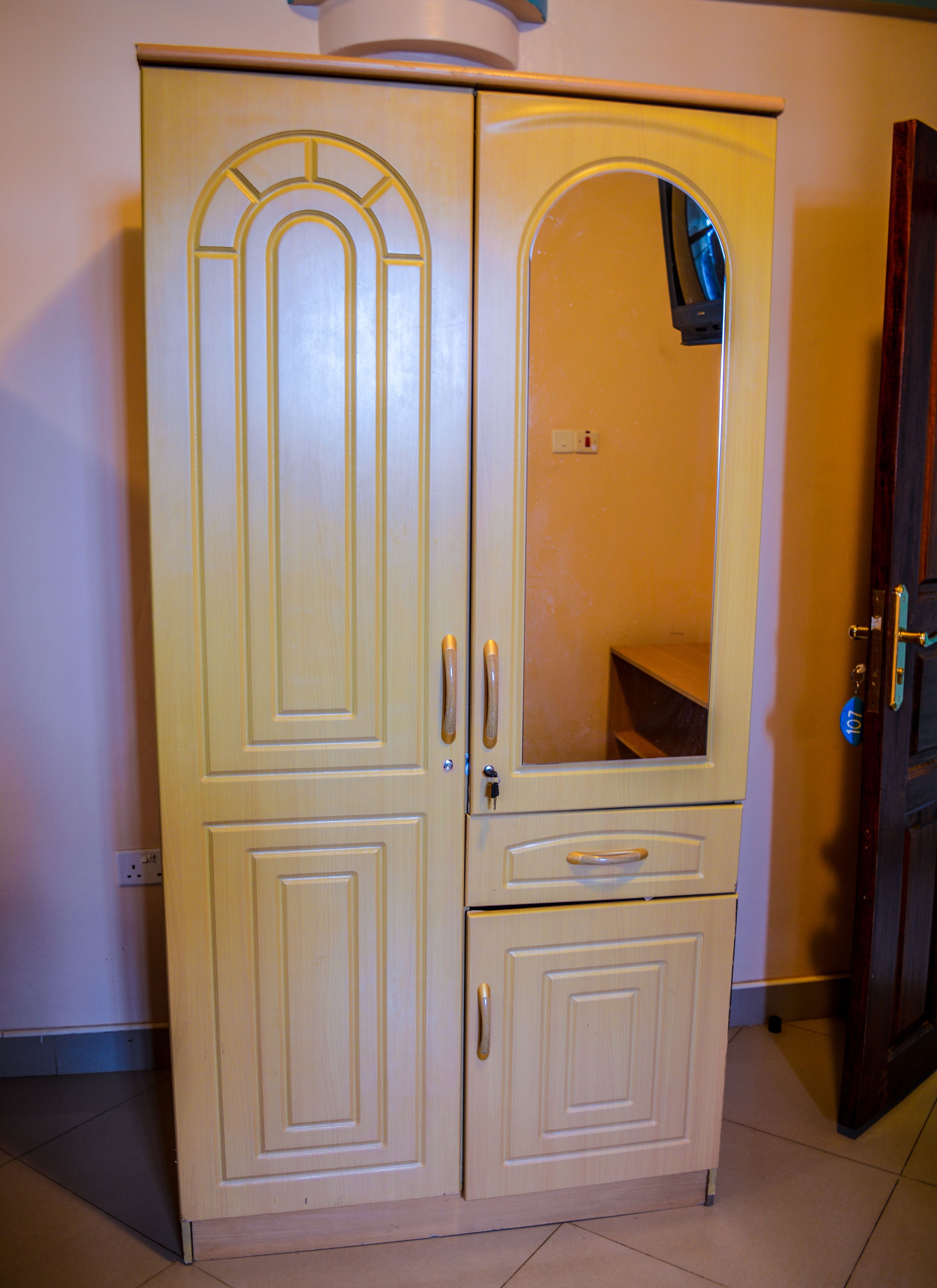 Un armario color crema con dos puertas, un espejo y un cajón pequeño.