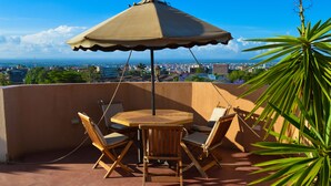 A terrace with a round wooden table and four chairs, a beige umbrella, and a view of a cityscape. - Stardom Hotel (Nairobi)