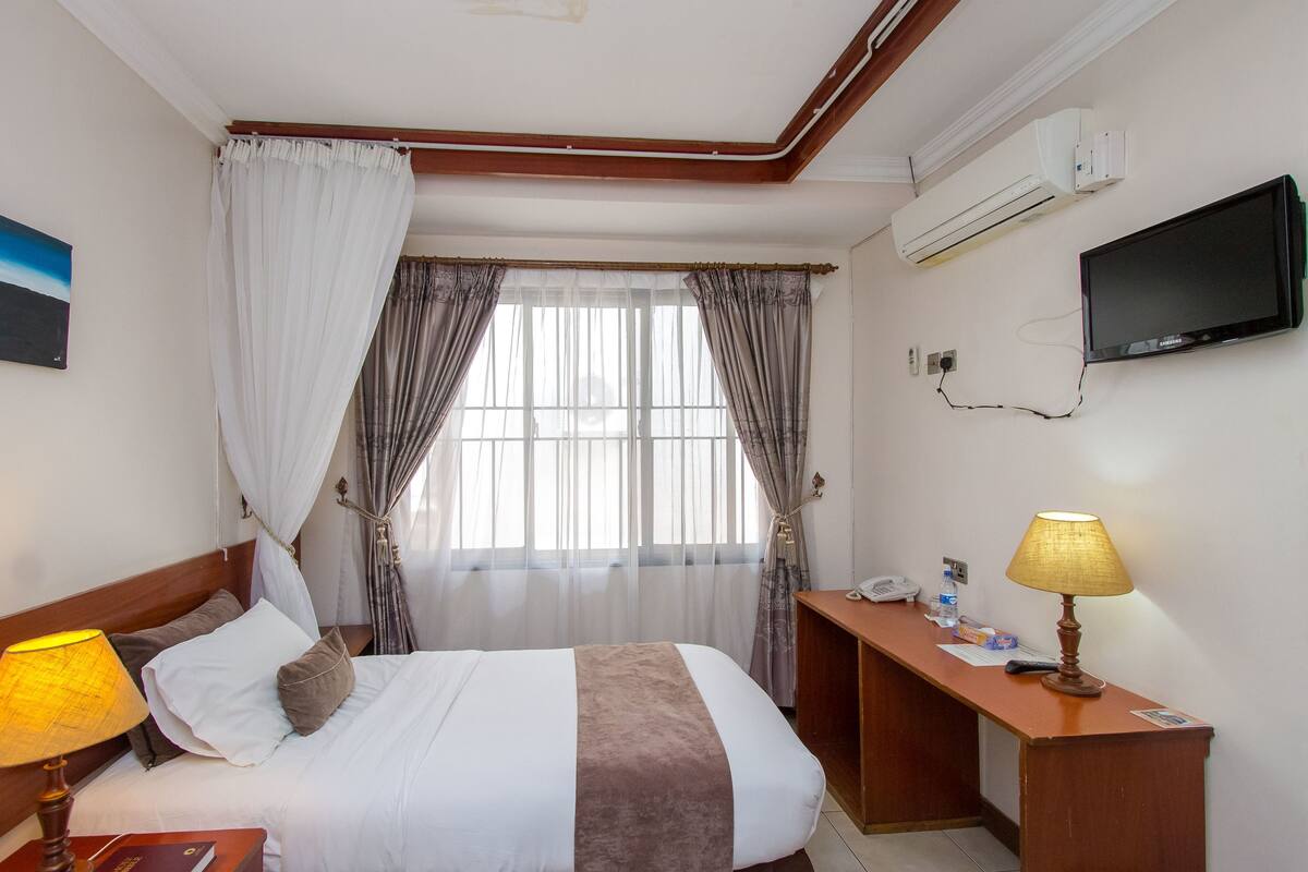 Una habitación de hotel con cama, escritorio, televisor y aire acondicionado.