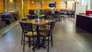 Een restaurant met houten wanden, meerdere tafels en stoelen, een aan de muur bevestigde televisie en een plant in een pot op een tafel.