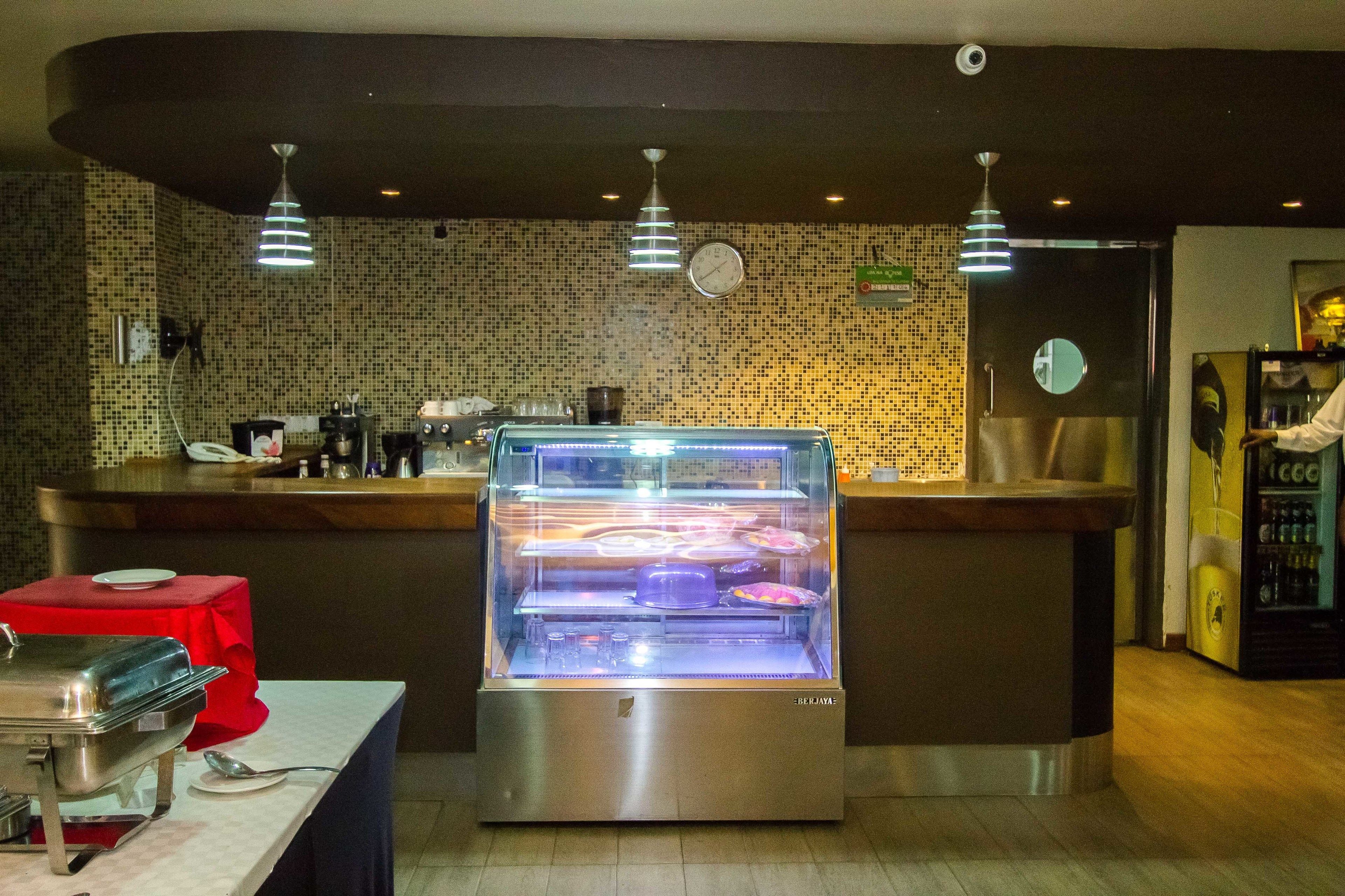 Zona de buffet con vitrina de vidrio, máquina de café y refrigerador.